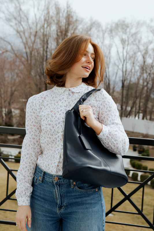 A woman wearing a floral white button up shirt with jeans and a black Drury Road Olivia Convertible Slouchy Tote Bag for Women over her shoulder.