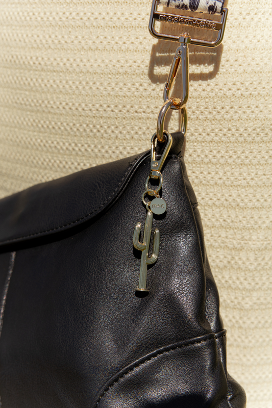Black leather bag with a cactus charm on a beige textured background