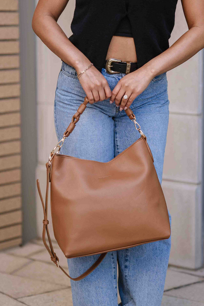 Woman holding a camel Drury Road Sawyer Convertible Slouchy Tote Bag for Women with a vegan leather braided shoulder strap as an adjustable crossbody strap hangs. 