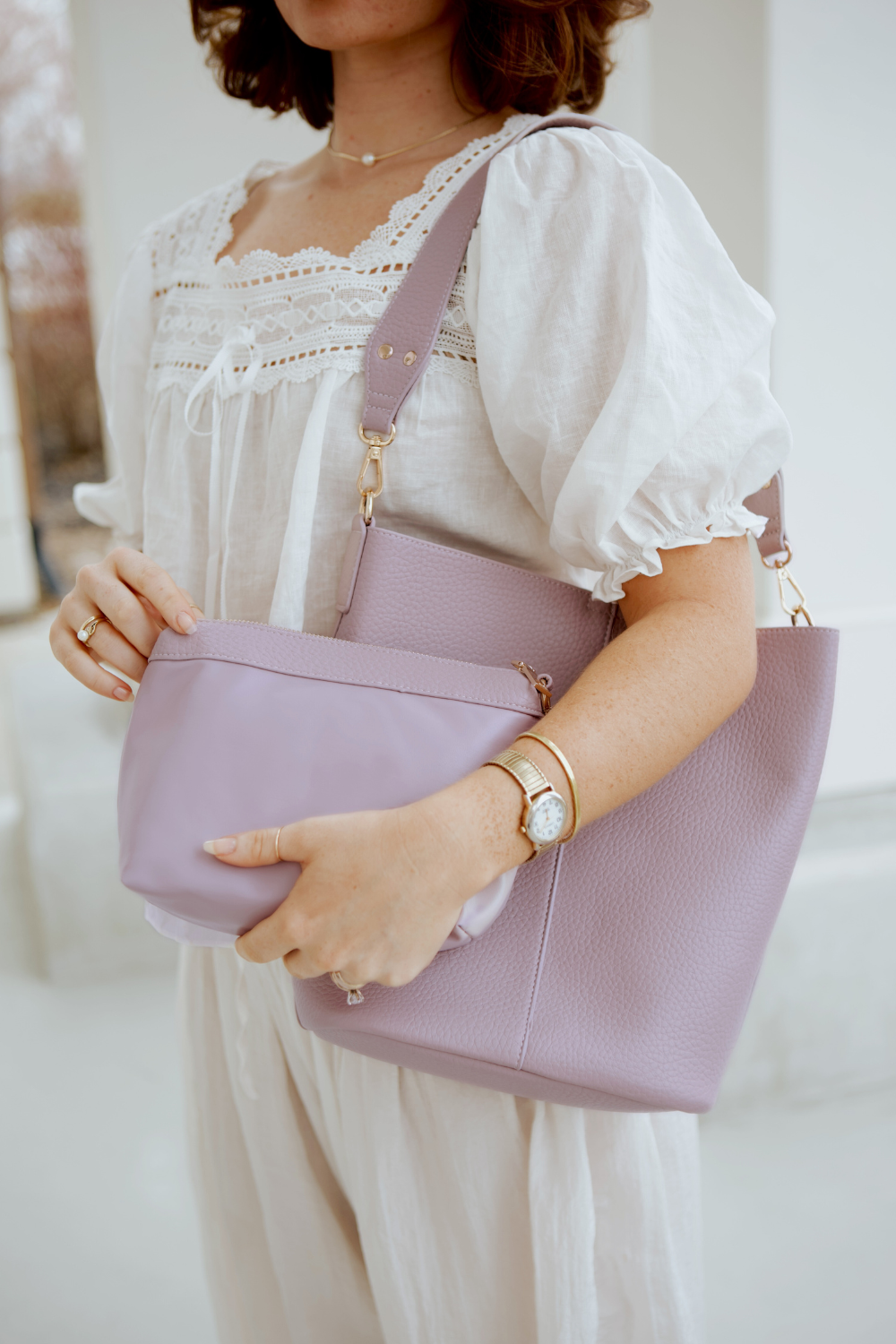 A woman holding a light violet Drury Road vegan leather Sophie Bucket Bag and coordinating zipper pouch for Women –  with a blurred background.
