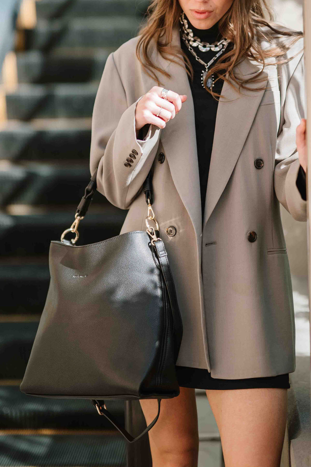 Woman holding a black Drury Road Sawyer Convertible Slouchy Tote Bag for Women with a vegan leather braided shoulder strap as a longer crossbody strap hangs. 