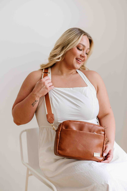 A blond haired woman modeling a camel colored Drury Road Alice Crossbody Vegan Leather bag. 