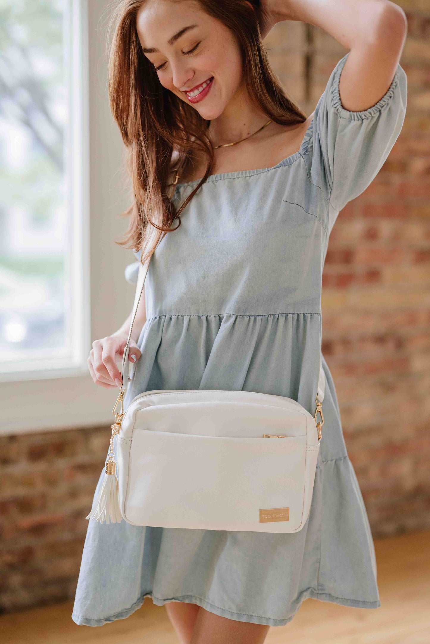 Red-haired woman wearing a white Drury Road Alice Crossbody vegan leather bad with gold hardware over her shoulder. 