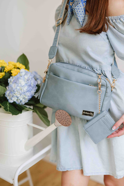A red-haired woman modeling a Drury Road Dusty Blue Alice Crossbody Bag: Vegan Leather Bag, Key Leash & Wallet