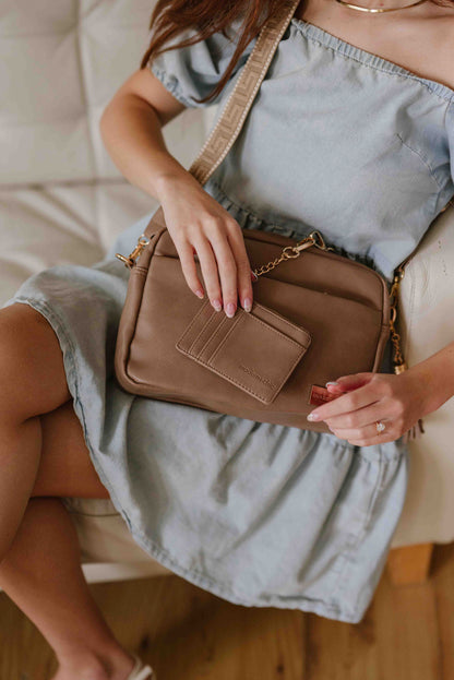 A red-haired woman modeling a Fawn colored Drury Road Alice Crossbody bag, showing the included key leash and wallet. 