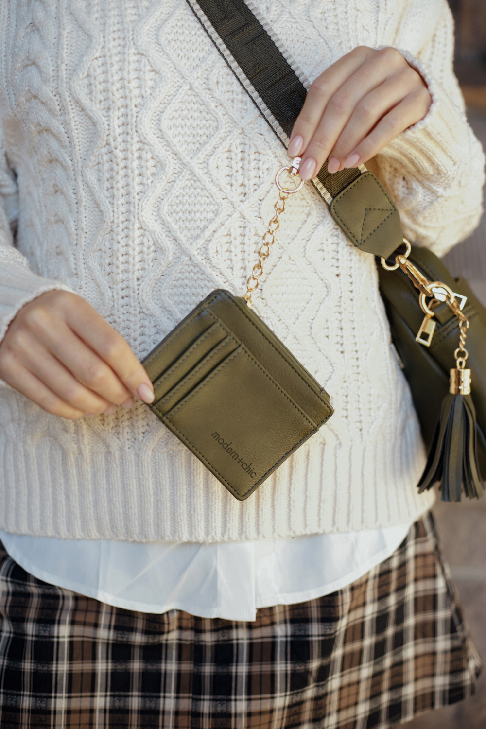 Person modeling an olive green Drury Road Alice Crossbody Vegan Leather bag holding a matching wallet with attached key leash. 