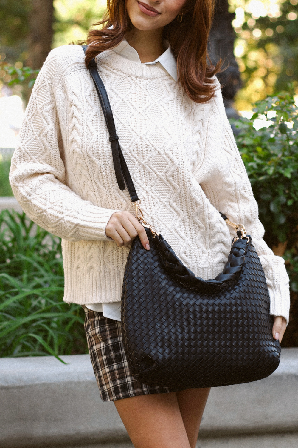 Woman holding a black Drury Road Kelly Woven Convertible Crossbody Shoulder Bag with included vegan leather adjustable crossbody strap outdoors.