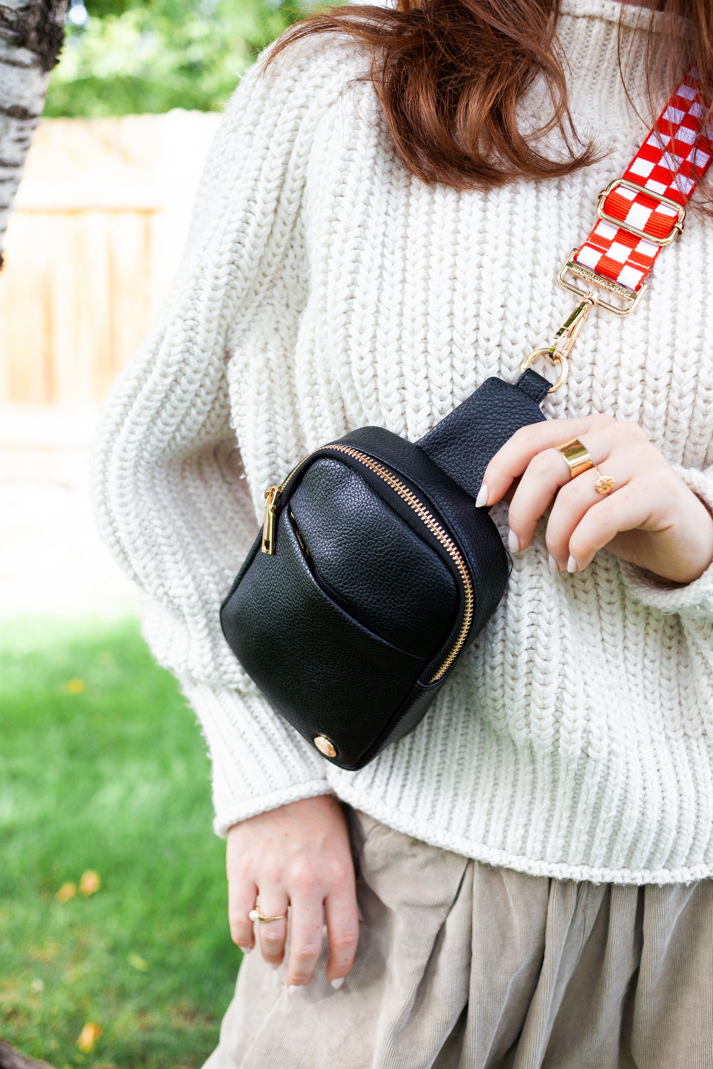 Woman wearing a red and white Drury Road Lizzie adjustable strap for crossbody bags on a black bag crossbody. 