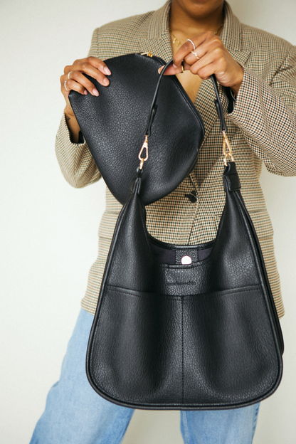 Person holding A black Drury Road Clara Vegan Leather Slouchy Tote Bag for Women with coordinating removable zipper pouch against a neutral background.