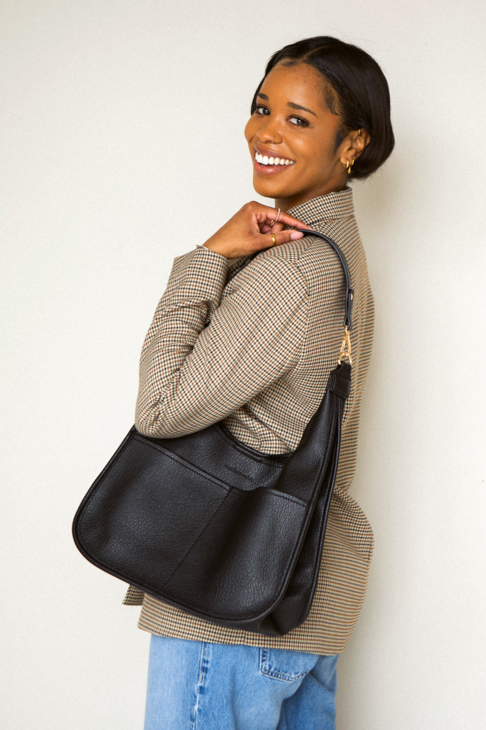 Woman holding a black  Drury Road Clara Vegan Leather Slouchy Tote Bag for Women on a white background. 