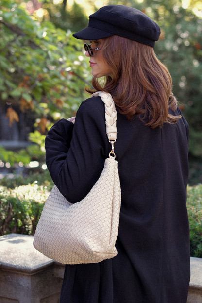 Woman in black coat and cap holding an ivory Drury Road Kelly Woven Convertible Crossbody Shoulder Bag outdoors.