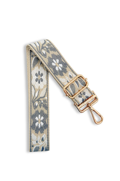 Grey floral patterned bag strap with gold hardware on a white background