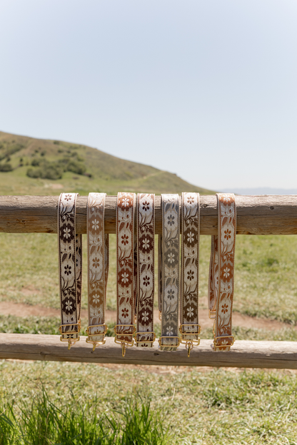 Daisy-themed bag straps with floral patterns hanging on a wooden fence with a scenic background.