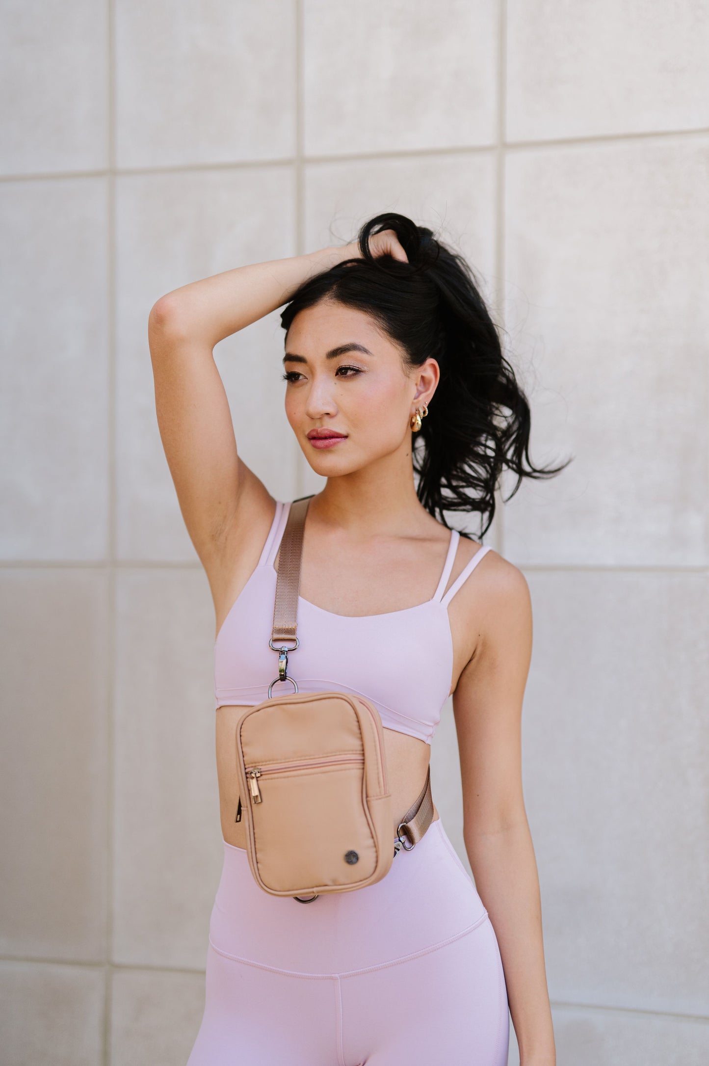 A woman wearing a pink sports bra and leggings showing a Drury Road Lainey Convertible Crossbody Bag for Women on crossbody. 