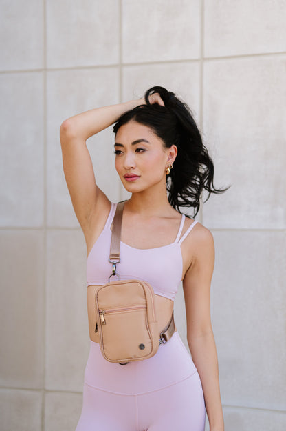 A woman wearing a pink sports bra and leggings showing a Drury Road Lainey Convertible Crossbody Bag for Women on crossbody. 