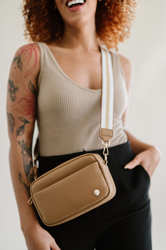 A woman wearing a camel colored Drury Road Willow Vegan Leather Convertible Crossbody Bag on a white background. 