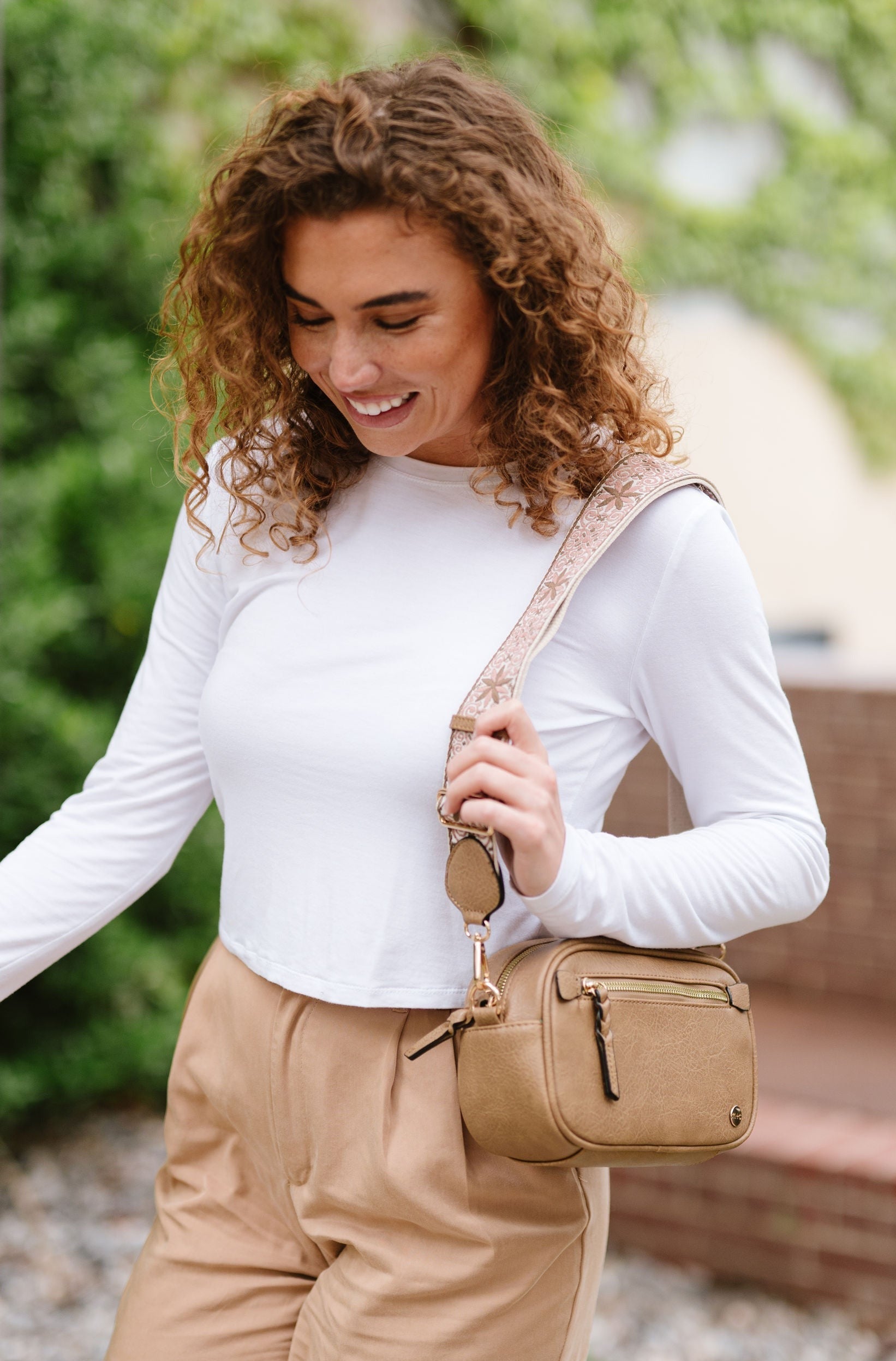 Woman wearing white shirt, tan pants and a Drury Road Gentry Vegan Leather Crossbody Bag in tan.