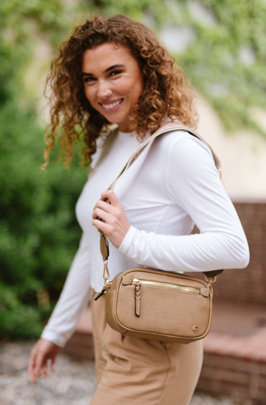 Woman wearing white shirt, tan pants and a Drury Road Gentry Vegan Leather Crossbody Bag in tan.
