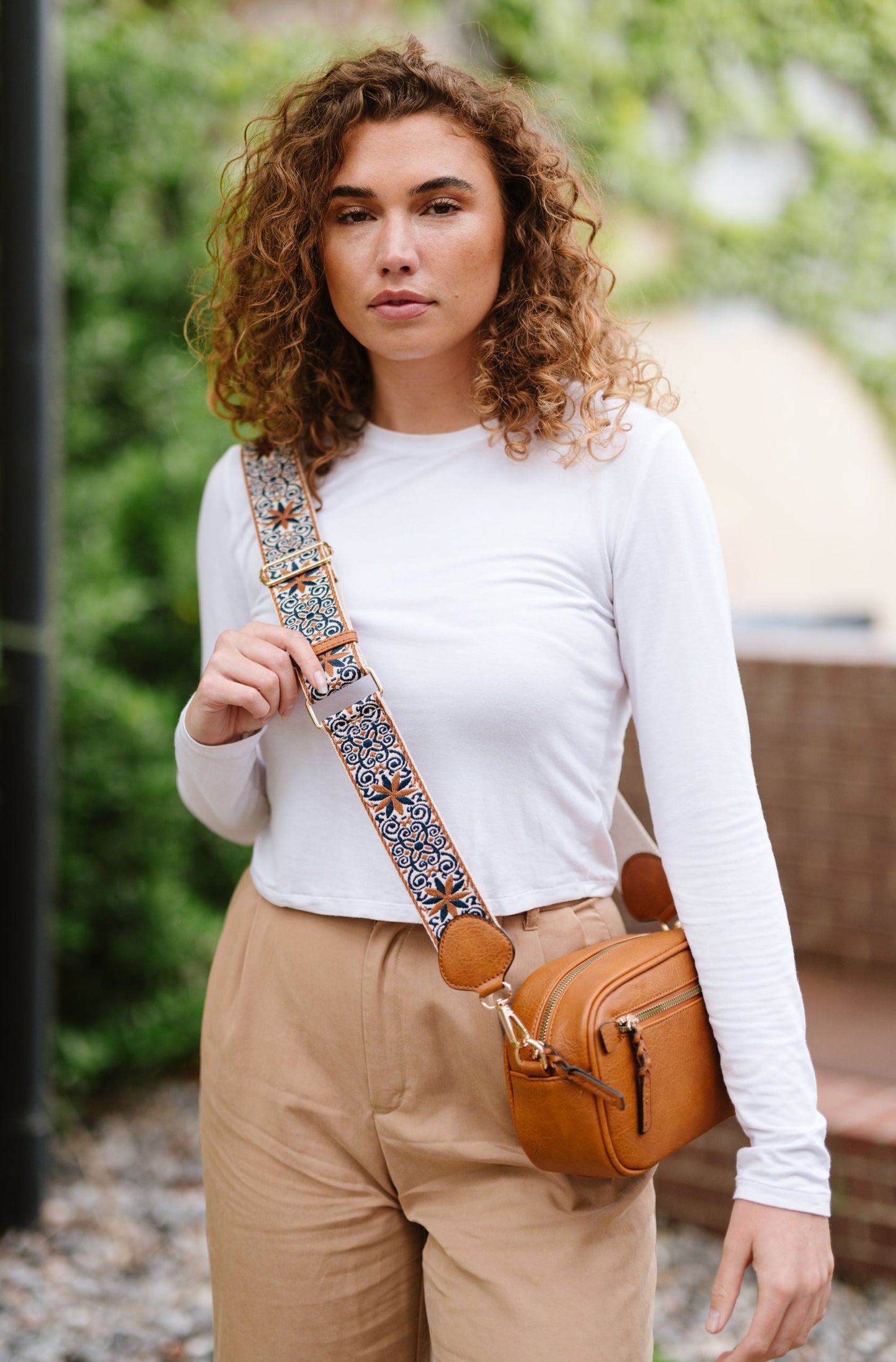 Woman wearing white shirt, tan pants and a Drury Road Gentry Vegan Leather Crossbody Bag in camel. 