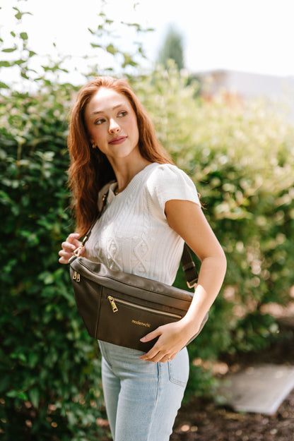 A woman wearing a cropped white sweater vest and an oversized olive Drury Road Presley Oversized Sling Bag for Women with gold hardware over her hip.
