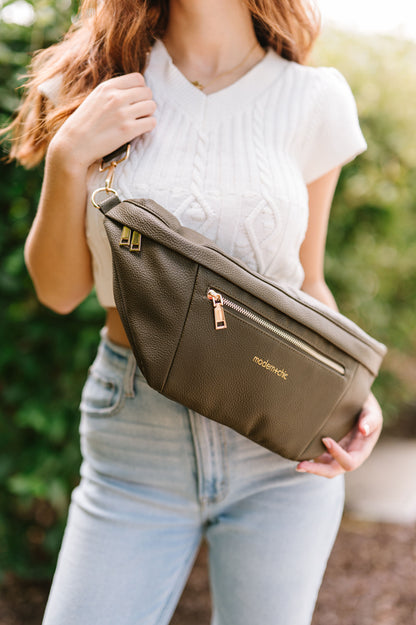 A woman wearing a cropped white sweater vest and an oversized olive Drury Road Presley Oversized Sling Bag for Women with gold hardware across her torso.