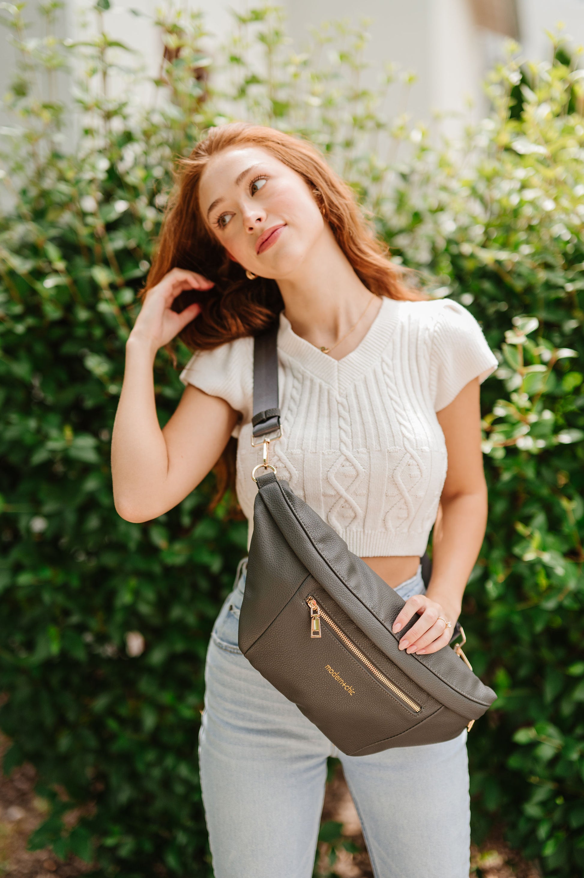 A woman wearing a cropped white sweater vest and an oversized olive Drury Road Presley Oversized Sling Bag for Women with gold hardware across her torso.