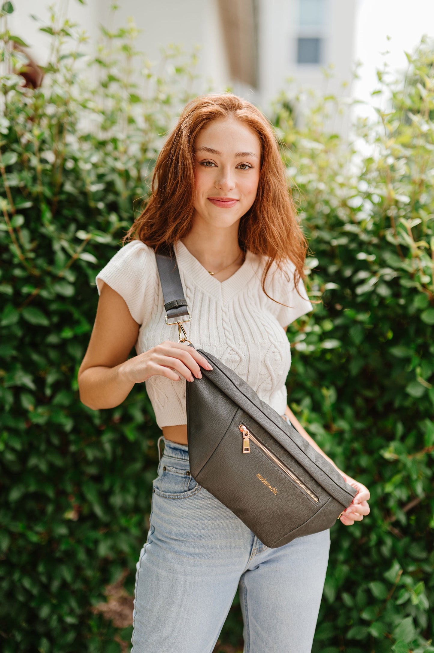 A woman wearing a cropped white sweater vest and an oversized olive Drury Road Presley Oversized Sling Bag for Women with gold hardware across her torso.