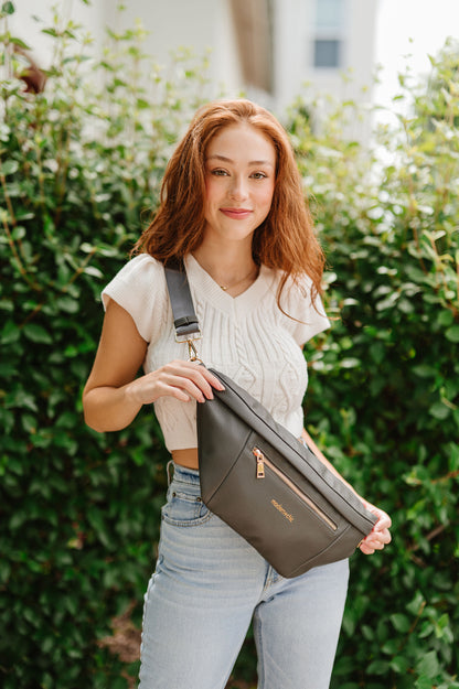 A woman wearing a cropped white sweater vest and an oversized olive Drury Road Presley Oversized Sling Bag for Women with gold hardware across her torso.
