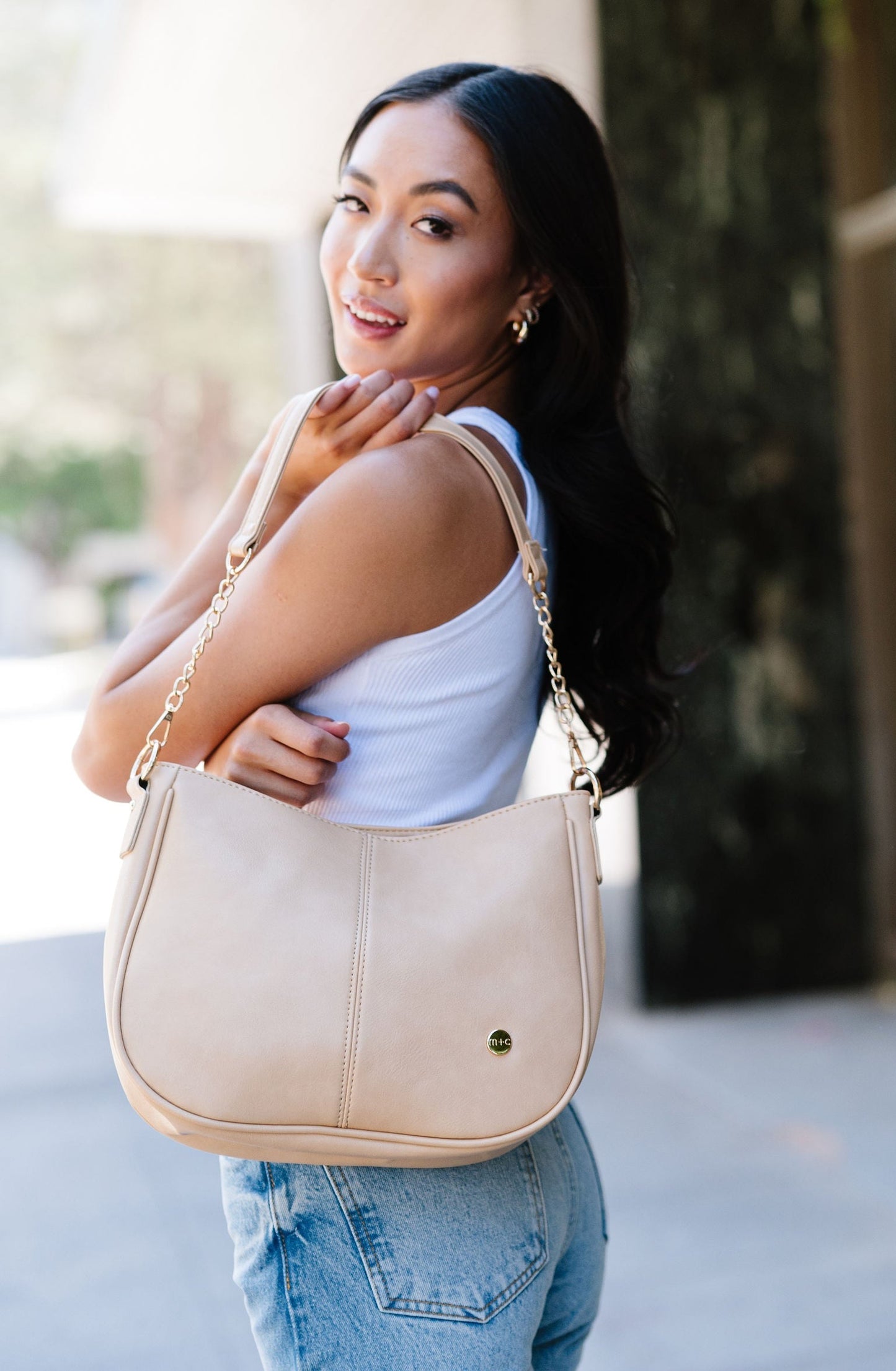 A woman wearing a cream Drury Road Marissa Vegan Leather Crossbody handbag over her shoulder displaying the gold chain accents on the strap.
