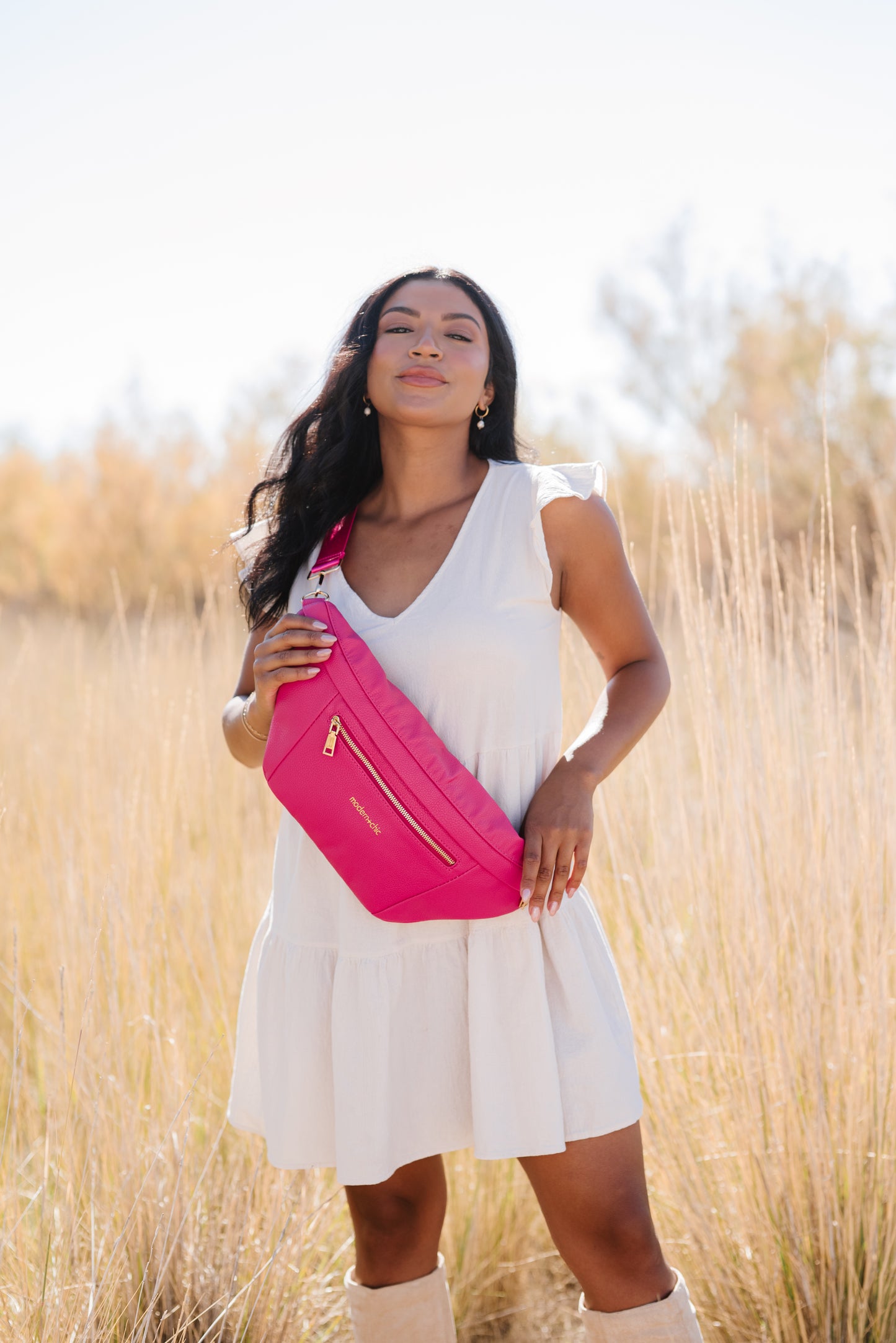 A woman wearing a white dress and a hot pink oversized Drury Road Presley Oversized Sling Bag for Women with gold hardware across her torso.