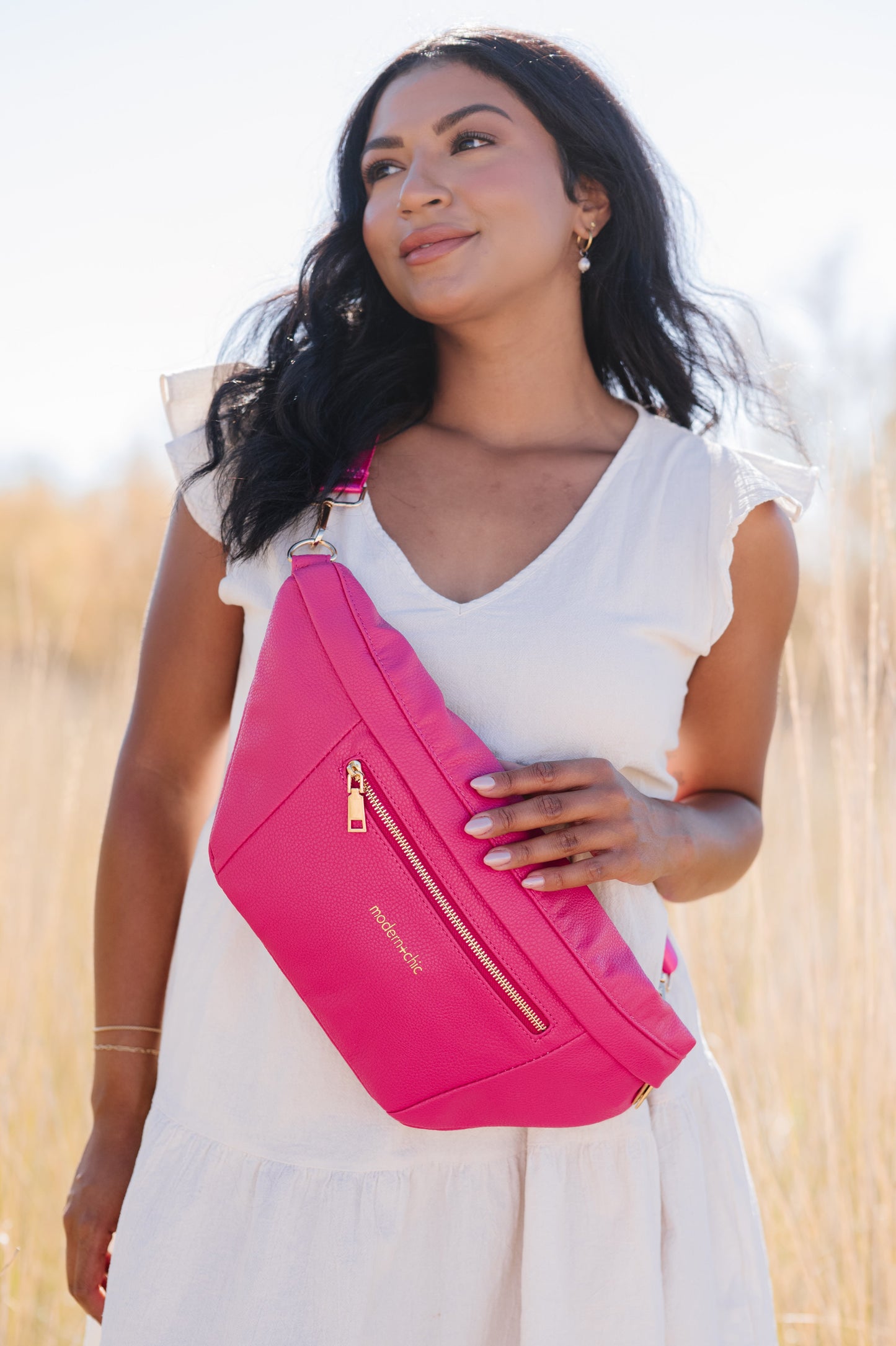 A woman wearing a white dress and a hot pink oversized Drury Road Presley Oversized Sling Bag for Women with gold hardware across her torso.