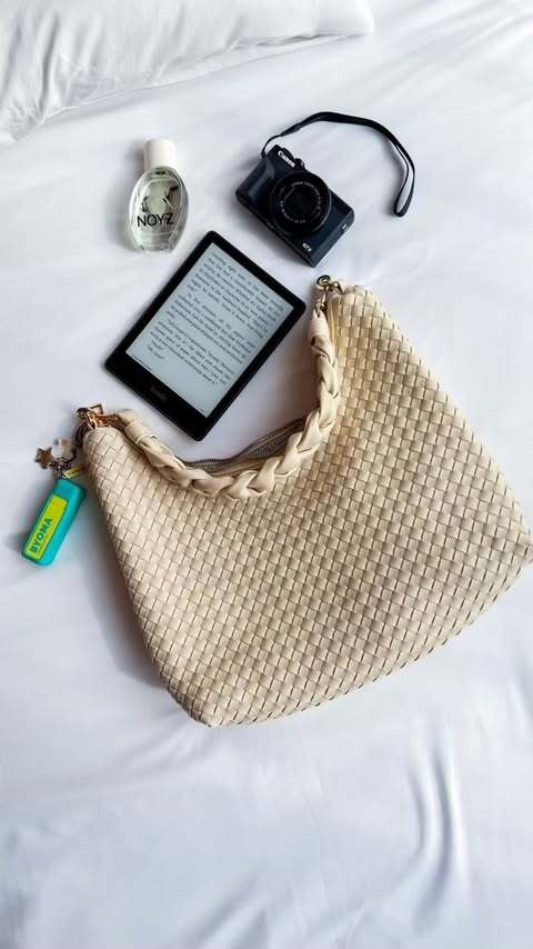 An ivory Drury Road Kelly Woven Convertible Crossbody Shoulder Bag with a variety of items including perfume, a camera and a kindle.
