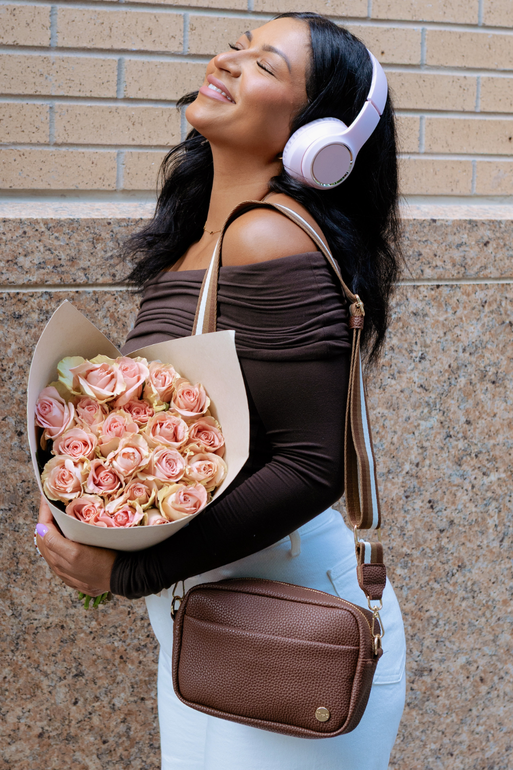 Woman wearing a brown Drury Road Willow Vegan Leather Convertible Crossbody Bag against a brick wall. 