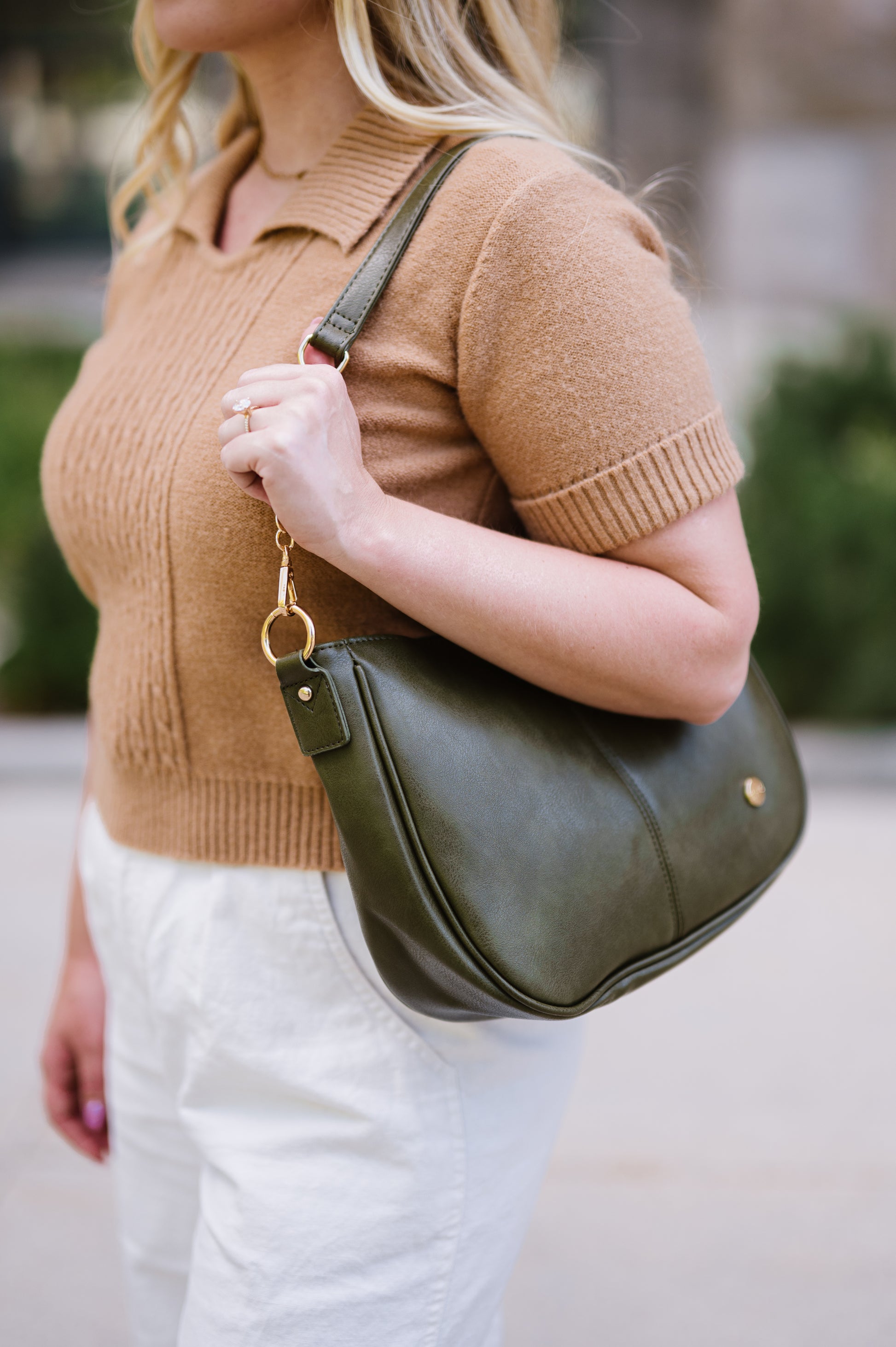 Woman holding an olive green Marissa Drury Road vegan leather crossbody handbag worn with a shorter strap as an over the shoulder handbag. 