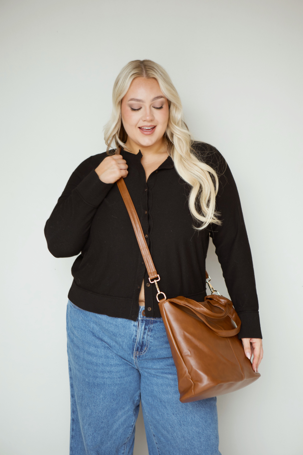 A woman wearing a black button up shirt with jeans and a brown Drury Road Olivia Convertible Slouchy Tote Bag for Women across her body. 