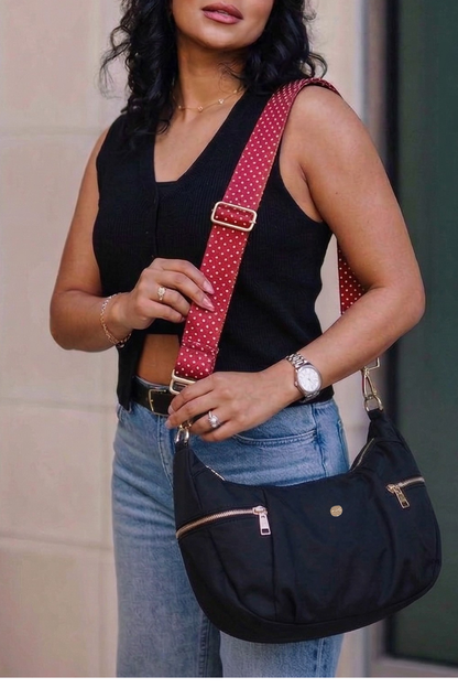 Woman holding a black Drury Road Parker Crescent Crossbody Bag for Women with a red polka dot strap.