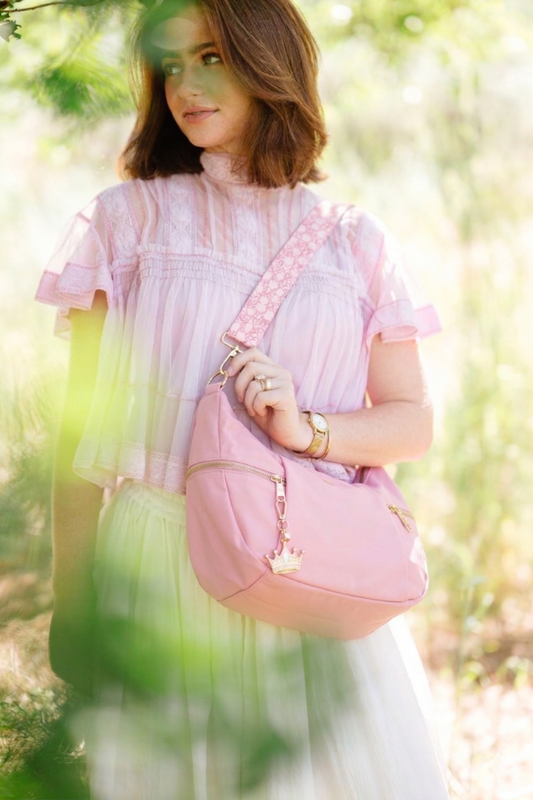 Woman holding a pink Drury Road Parker Crescent Crossbody Bag for Women in a forest setting.