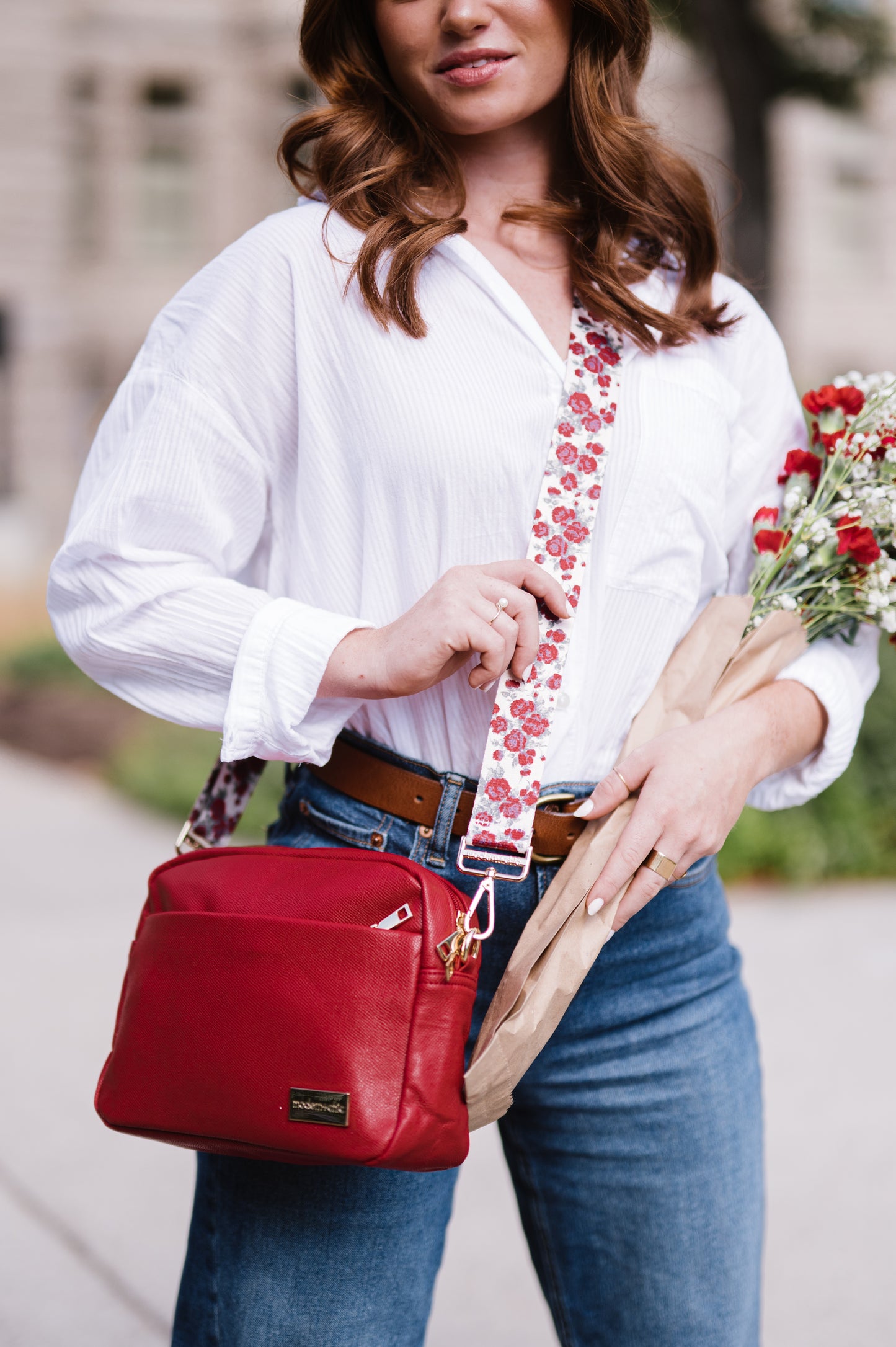 Woman holding a bouquet of flowers and a red bag with a floral strap.