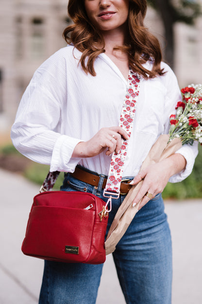 Woman holding a bouquet of flowers and a red bag with a floral strap.