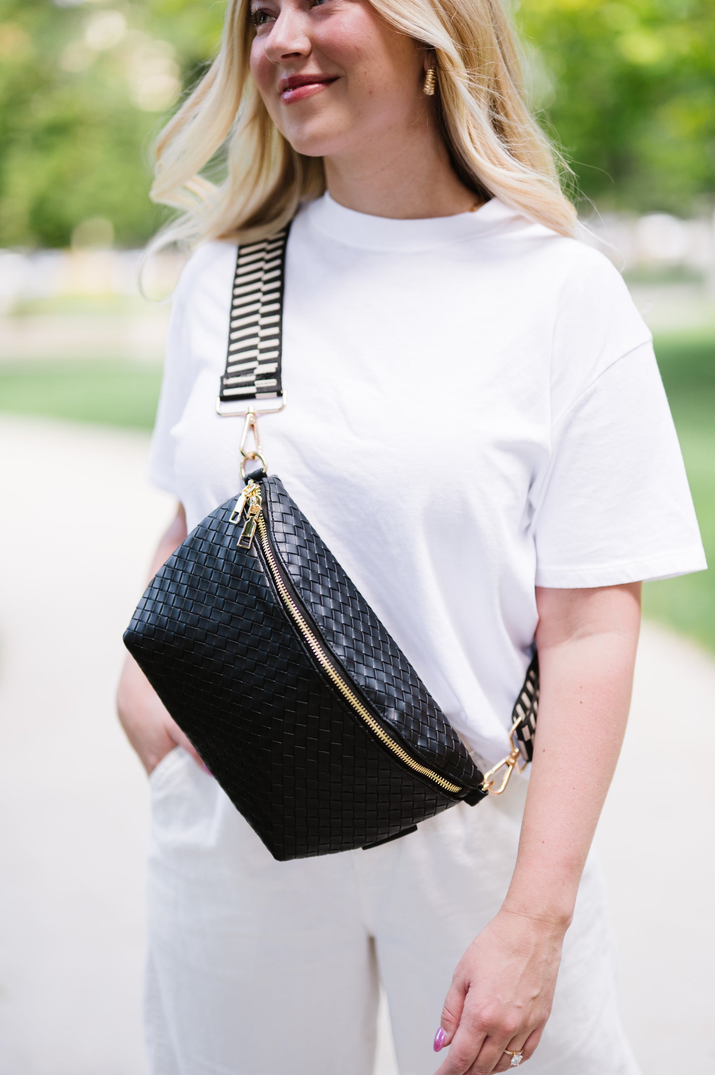 Woman wearing a white t-shirt and a black criss cross style Drury Road Rory Oversized Belt Bag for Women with a gold zipper and hardware crossbody.