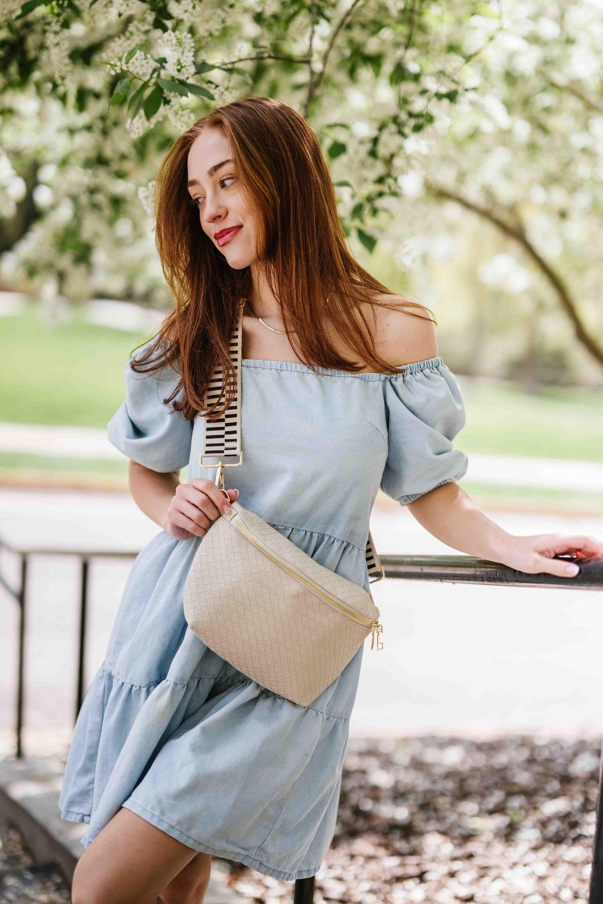 Woman wearing an off the shoulder blue dress and a cream criss cross style Drury Road Rory Oversized Belt Bag for Women with a gold zipper and hardware crossbody.