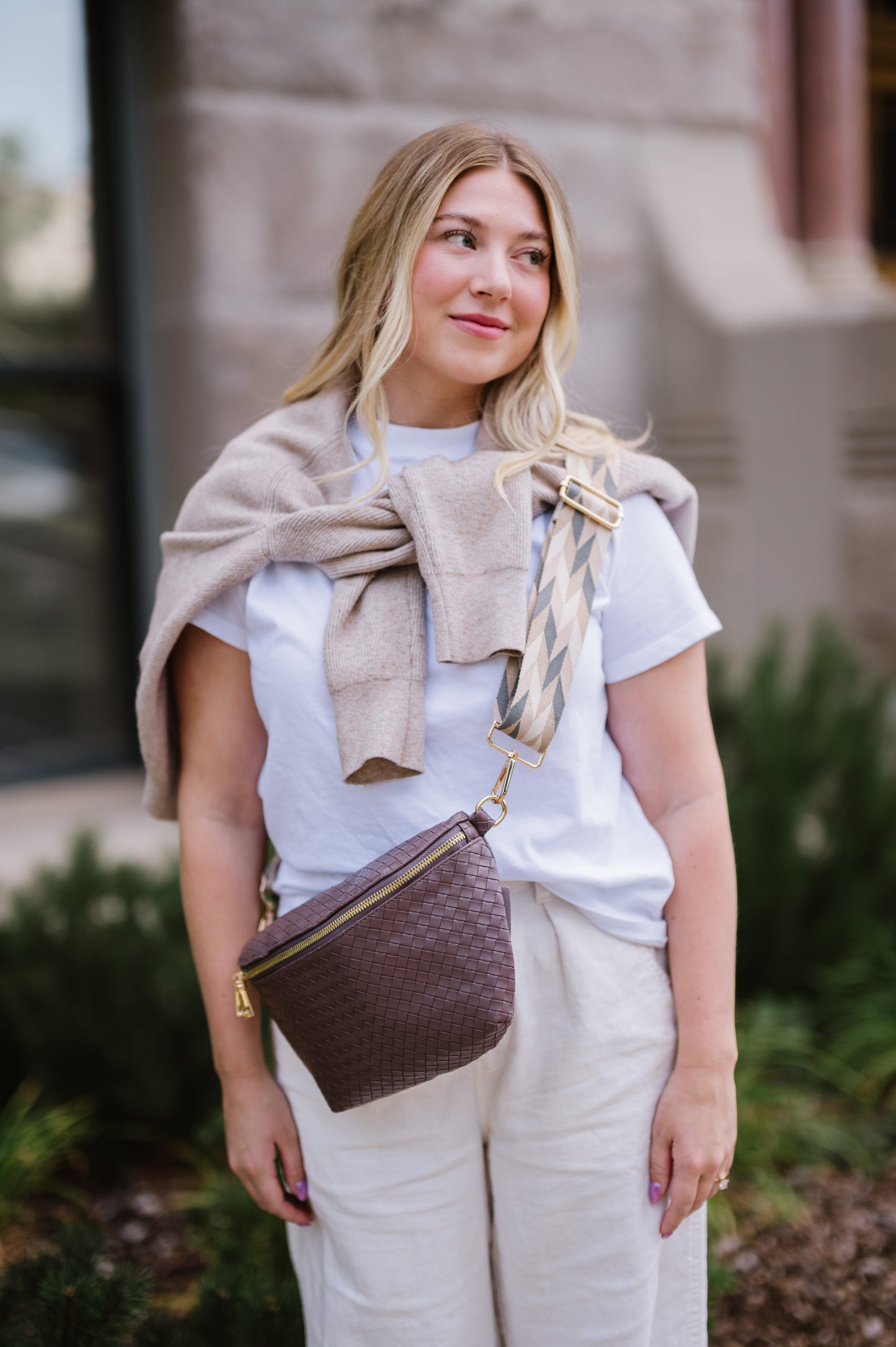 Woman wearing a white t-shirt, a sweatshirt tied around her shoulders and a brown criss cross style Drury Road Rory Oversized Belt Bag for Women with a gold zipper and hardware crossbody.