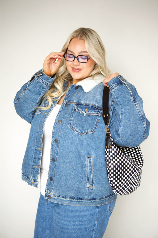 Woman wearing a denim jacket and jeans with a black vegan leather Drury Road Savannah Slouchy Tote on a white background. 