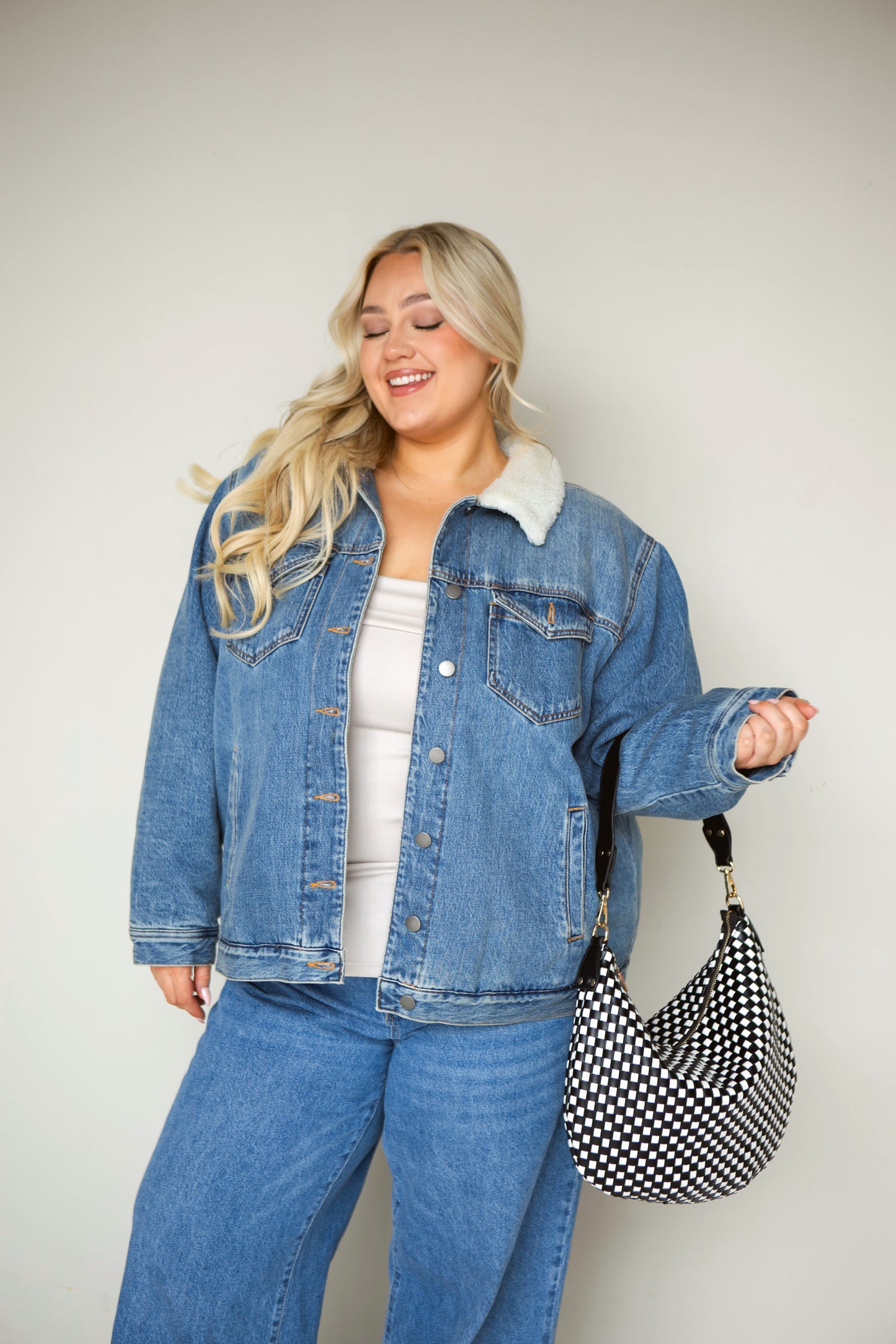Woman wearing a denim jacket and jeans with a black and white woven vegan leather Drury Road Savannah Slouchy Tote on a white background. 
