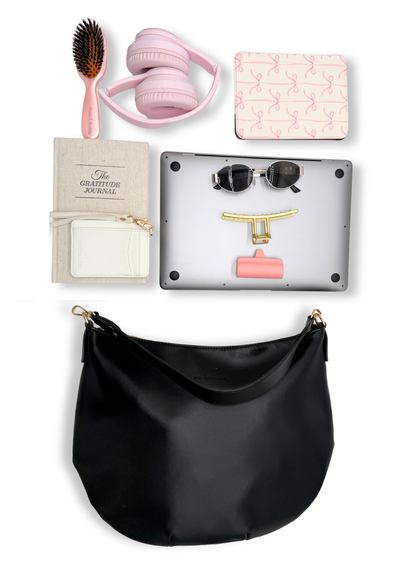 A black vegan leather Drury Road Savannah Slouchy Tote on a white background with pink accessories including headphones, a hairbrush, and a small notebook on a white background.
