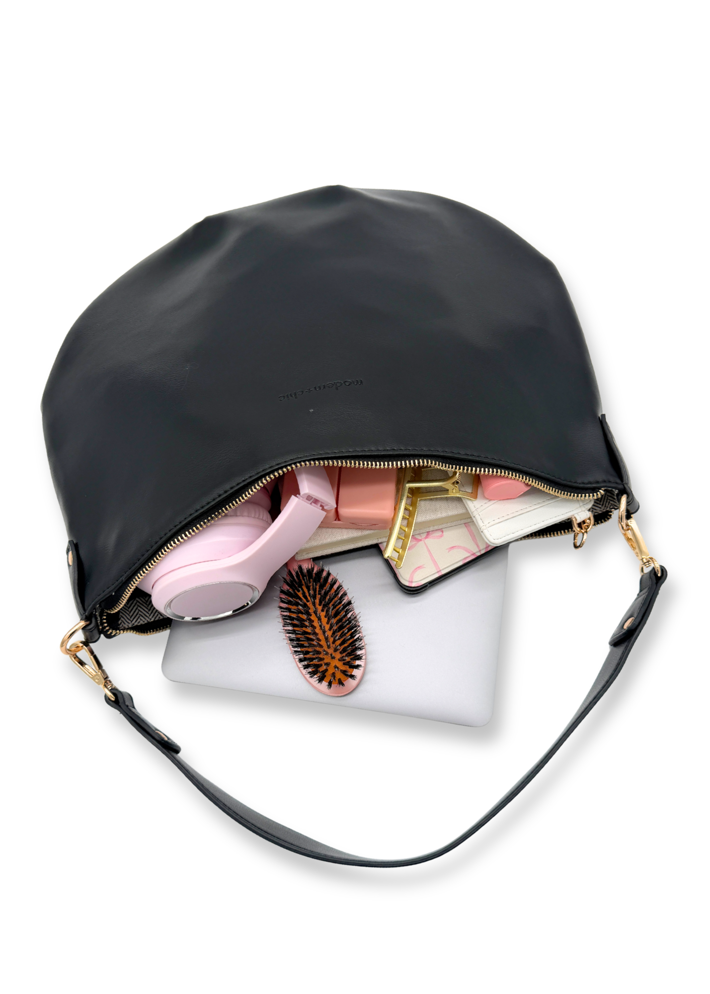 A black vegan leather Drury Road Savannah Slouchy Tote on a white background with a laptop, pink headphones, kindle and hairbrush on a white background. 