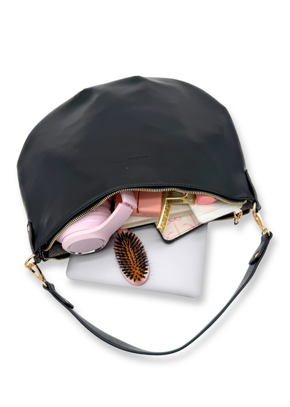 A black vegan leather Drury Road Savannah Slouchy Tote on a white background with a laptop, pink headphones, kindle and hairbrush on a white background. 