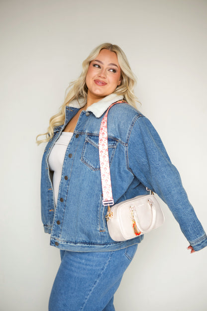 Woman wearing a denim jacket with a cream Drury Road Remi Vegan Leather Crossbody Purse with gold hardware, cream printed strip and charm. 