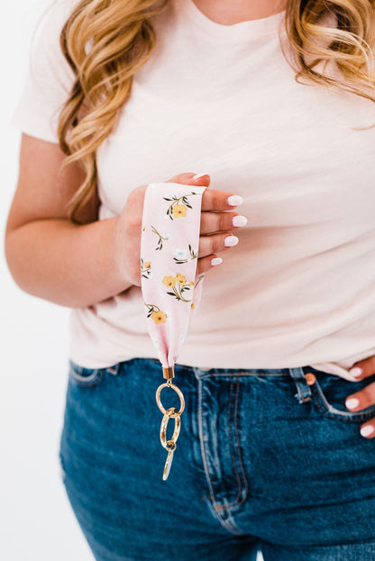 A woman wearing a white tee shirt and jeans holding a white floral printed Drury Road Luna Fabric Keychain Bracelet for Women.