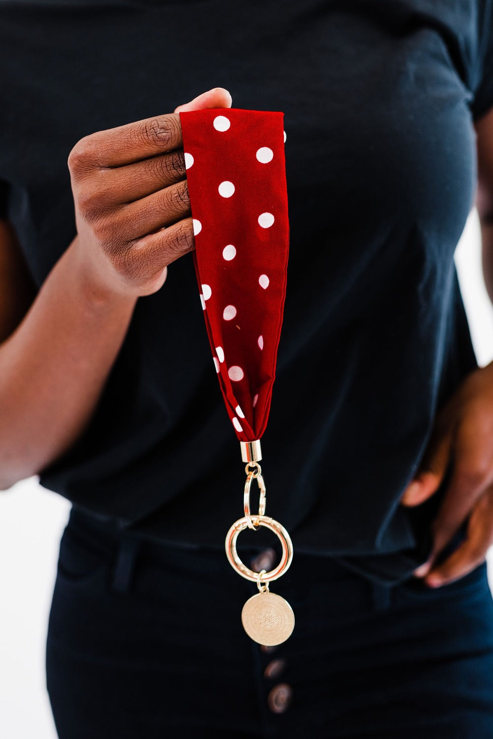A woman wearing all black holding a red and white polka dot Drury Road Luna Fabric Keychain Bracelet for Women her hand.